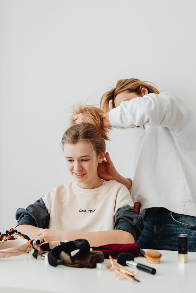 A mother assists her daughter with styling hair at home, capturing a warm family moment.